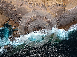 Aerial top view of sea waves hitting rocks on the beach with turquoise sea water. Amazing rock cliff seascape in the Portuguese co