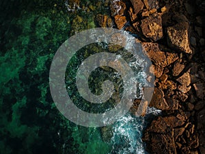 Aerial top view of sea waves hitting rocks on the beach with turquoise sea water. Amazing rock cliff seascape in the Portuguese co