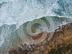 Aerial top view of sea waves hitting rocks on the beach with turquoise sea water. Amazing rock cliff seascape in the Portuguese co