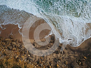 Aerial top view of sea waves hitting rocks on the beach with turquoise sea water. Amazing rock cliff seascape in the Portuguese co