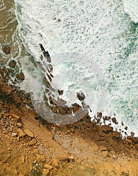 Aerial top view of sea waves hitting rocks on the beach with turquoise sea water. Amazing rock cliff seascape in the Portuguese co