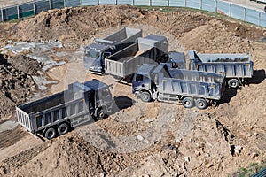 Aerial top view of several dump trucks unloading sand at a construction site. Industrial panorama.