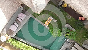 Aerial top view of slim young woman in beige bikini relaxing and get sunbathe near swimming pool in chaise-longue jungle