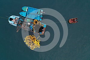 Aerial top view of a small blue colored fishing boat with a fishingnet floating alongside