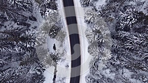 Aerial top view snowy forest mountains with cars driving winter road.