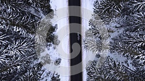 Aerial top view snowy forest mountains with cars driving winter road.