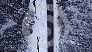 Aerial top view snowy forest mountains with cars driving winter road.