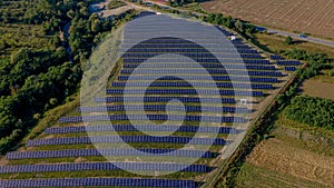 Aerial Top view on Solar Power Station in Green Field on Sunny day. Drone fly over Solar Farm. Lot of Solar Panels Stand in Row