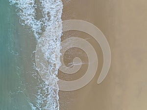 Aerial top view to tropical sandy beach and blue ocean. Top view of ocean waves reaching shore on sunn