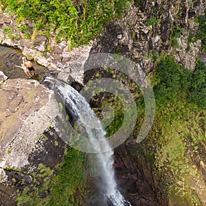 Aerial top view of travel couple waving to drone, standing on the edge of 500 feet waterfall in the tropical island