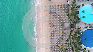 Aerial top view on tropical island beach. Umbrellas, sand and sea waves