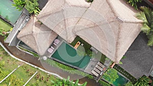 Aerial top view of villa with straw roofs with swimming pool and slim young woman in beige bikini relaxing and get