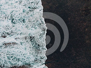 Aerial top view of waves crashing against stone rocks