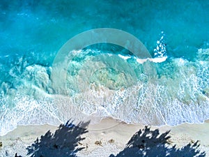 Aerial top view of the waves crashing on the beach with a shadow of trees in Waimanalo, Oahu, Hawaii