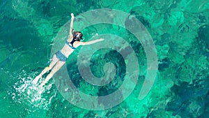 Aerial top view of woman snorkeling from above, girl snorkeler swimming in a clear tropical sea water with corals