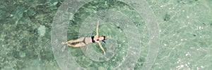 Aerial top view of woman snorkeling from above, girl snorkeler swimming in a clear tropical sea water with corals during