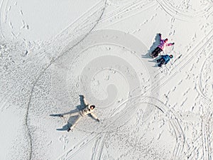 Aerial top view young adult mother cute little sibling kids boy girl have fun play make snow angel white frozen lake ice