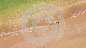 Aerial top view of young woman in bikini relaxing on sand tropical beach by sea and waves from above, girl on tropical island