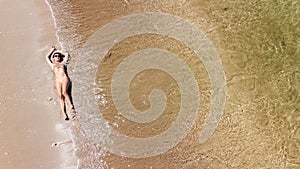 Aerial top view of young woman in bikini relaxing on sand tropical beach by sea and waves from above, girl on tropical island