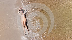 Aerial top view of young woman in bikini relaxing on sand tropical beach by sea and waves from above, girl on tropical island