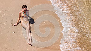 Aerial top view of young woman in bikini relaxing on sand tropical beach by sea and waves from above, girl on tropical island