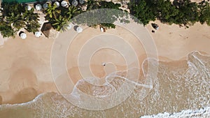 Aerial top view of young woman in black swimwear lying on sandy shore with surfboard. Pretty surfer girl relax after