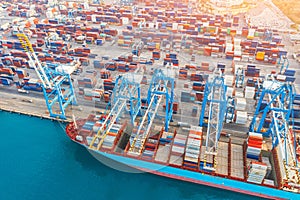 Aerial tope view - heavy huge ship with a lot of containers moored at the pier in the port, loading with cranes in the industrial