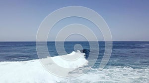 Aerial tracking shot of a surfer riding big surf waves in deep blue ocean at day