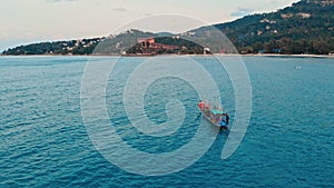 Aerial tracking small fishing boat motoring in Costa Rica bay at speed with tropical mountains background. Wide top view