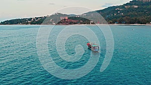 Aerial tracking small fishing boat motoring in Costa Rica bay at speed with tropical mountains background. Wide top view