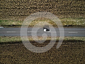 Aerial Tranquility: White Car on a Straight Rural Road Amidst Dried Cornfields
