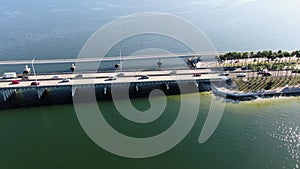 Aerial trucking shot over blue bay water and palm trees over bridge with traffic