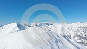 AERIAL: Unrecognizable skier reaches the summit of a snowy mountain in the Alps.