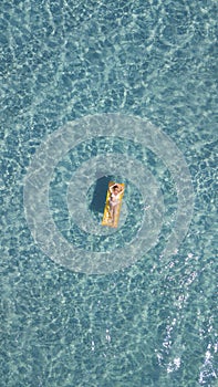 Aerial vertical view of woman relaxing and enjoying summer holiday vacation laying on a colorful inflatable lilo mattress on blue