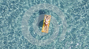 Aerial vertical view of woman relaxing and enjoying summer holiday vacation laying on a colorful inflatable lilo mattress on blue