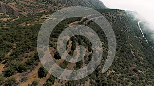 Aerial viAerial view of green hills and bushes on cloudy sky background. Shot. Flying above beautiful mountain top and
