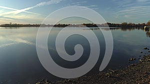 Aerial video, coming out of the woods unto the shore near a river at sunset with blue sky