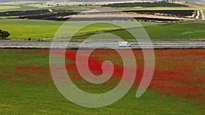 Aerial video of a highway between a poppy field with vibrant red color and a solar panel plant in Spain