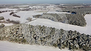 Aerial video view of a winter landscape in Europe, flying over small forests toward a small village