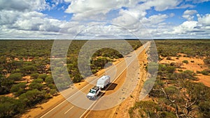 Aerial view of 4WD and modern caravan on an outback highway in Australia under a blue cloudy sky