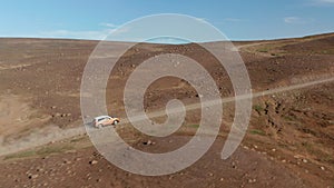 Aerial view 4x4 car driving climbing rocky hill in desert landscape in Iceland. Birds eye view of vehicle stirring up