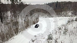 Aerial view of a 6x6 SUV, which rides on a snow-covered road in winter forest