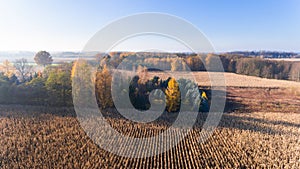 Aerial view from above of corn field after harvest, forest and farmland in autumn sunset