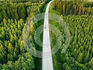 Aerial view from above of country road through the green summer forest in summer Finland.