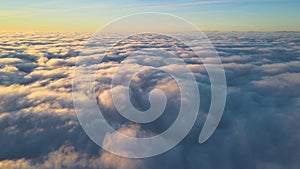 Aerial view from above at high altitude of dense puffy cumulus clouds flying in evening. Amazing sunset from airplane