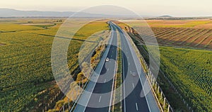 Aerial view above highway road, travel cars and agricultural fields at sunset