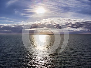 Aerial view above ocean, with  cloudy pastel colored scenic sky and  sun rays hits the water in a hot summer day