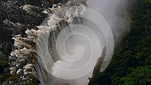 Aerial view in abysm of Victoria Falls and rainforest with enormous water spray at the end of rainy season from helicopter.