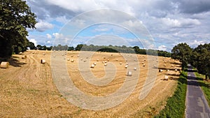 Aerial view of an agricultural field with numerous hays on it surrounded by green trees