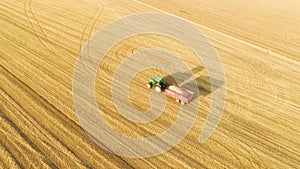 Aerial view of agricultural tractor with cargo cart in field. Beautiful sunset.